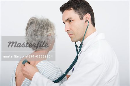 Mid adult doctor checks breathing of senior patient