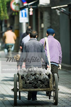 Chine, Beijing. Hommes transportant des briques de charbon de bois dans un quartier Hutong.