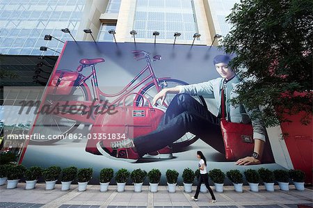 China,Beijing. A young woman walking past a giant poster of a Gucci advert