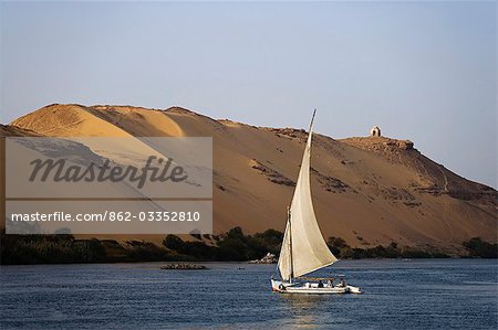 A felucca sails along the Nile at Aswan,Egypt,the desert stretching away behind.