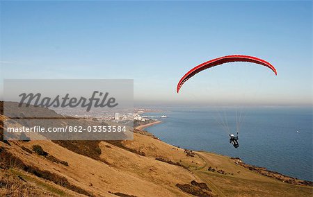 England,East Sussex,Eastbourne. Paragliding is a recreational and competitive flying sport. A paraglider is a free-flying,foot-launched aircraft. The pilot sits in a harness suspended below a fabric wing,whose shape is formed by the pressure of air entering vents in the front of the wing.