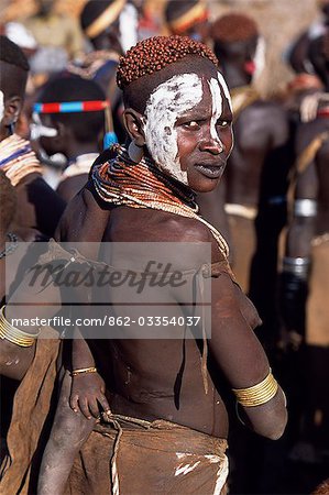 A Karo mother carries her baby on her hip. She has decorated herself with face paint,a hairdo styled with mud and ochre and layers of beads and amulets. A small Omotic tribe related to the Hamar,who live along the banks of the Omo River in southwestern Ethiopia,the Karo are renowned for their elaborate body painting using white chalk,crushed rock and other natural pigments.