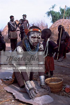 A Nyangatom woman grinds sorghum using two stones. Typical of her tribe,she wears a heavily beaded calfskin skirt,multiple layers of bead necklaces and metal bracelets and amulets. The Nyangatom or Bume are a Nilotic tribe of semi-nomadic pastoralists who live along the banks of the Omo River in south-western Ethiopia.