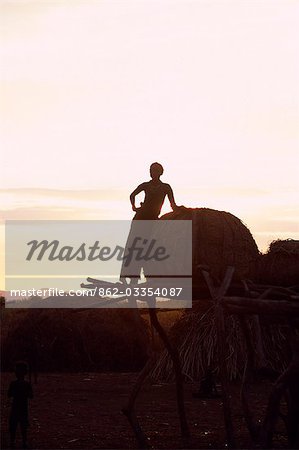 A Dassanech girl leaning against a bale of cattle fodder on a raised platform is silhouetted against the evening sky at a settlement alongside the Omo River. Much the largest of the tribes in the Omo Valley numbering around 50,000,the Dassanech (also known as the Galeb,Changila or Merille) are Nilotic pastoralists and agriculturalists.