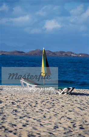 Transat parasol et le soleil sur la plage près de Corralejo avec les pics de Lanzarote dans le lointain