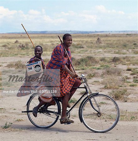 Alt und neu. Traditionell gekleidet und tragen vertraut Holzstab, geben zwei junge Männer Hinweise, die der Lebensstil der jüngeren Generationen der Masai in Tansania allmählich geändert wird.