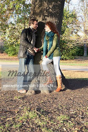 A couple stand face to face next to a tree