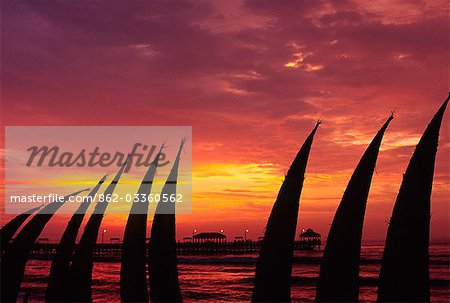 The setting sun paints the sky red,silhouetting totora (reed) boats stacked on the beachfront at Huanchaco,in northern Peru. The boats are the traditional craft of the local pescadores (fishermen).