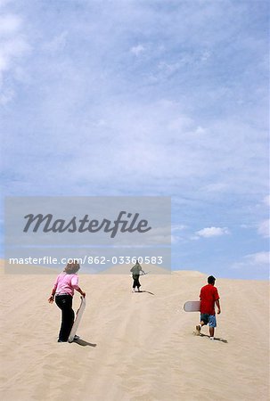 A family scales the dunes for some sandboarding,near the Huacachina in southern Peru. The oasis village of Huacachina is a popular destination for its desert adventure activities.