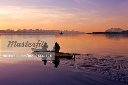 Kayakers paddle the calm waters of Alaska's Inside Passage with Herbert Glacier in the background at sunset, Tongass National Forest near Eagle Beach State Recreation Area.