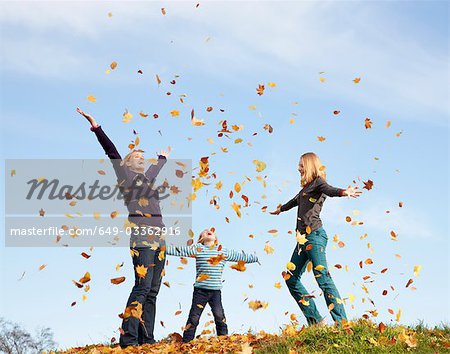 woman, boy and girl throw autumn leaves