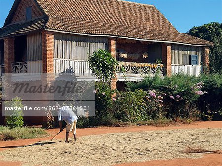 Un homme propage de riz pour le séchage à l'extérieur d'une maison typique de hautes terres du sud du Madagascar.