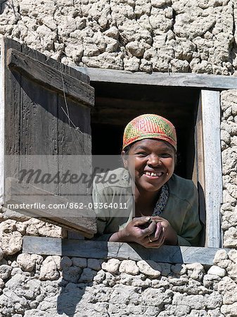 Une jeune fille portant un chapeau tressé malgache peeps par la fenêtre à l'étage de sa maison près de Ambalavao, Madagascar
