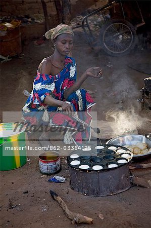 Mali,Bamako,Tinan. A Woman cooks muffins on a wood stove beside the road at the busy weekly market of Tinan situated between Bamako and Segou.