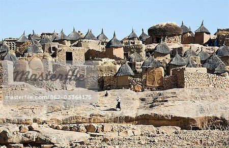 Mali, pays Dogon. Un joli village Dogon au sommet de l'escarpement de Bandiagara. Le toguna ou réunion maison des hommes est l'en forme de dôme de bâtiment sur la ligne d'horizon avec l'herbe séchée sur le toit. Habitations ont des toits plats alors que les greniers carrés ont planté des toits de chaume. Mali, pays Dogon. Un joli village Dogon au sommet de l'escarpement de Bandiagara. Le toguna ou réunion maison des hommes est l'en forme de dôme de bâtiment sur la ligne d'horizon avec l'herbe séchée sur le toit. Habitations ont des toits plats alors que les greniers carrés ont planté des toits de chaume.