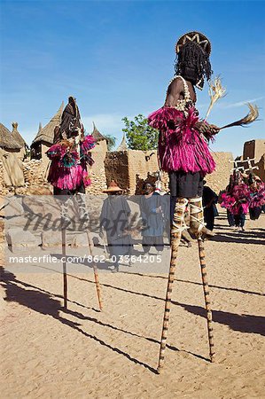 Mali,Dogon Country,Tereli. Masked stilt dancers wearing coconut shells as breasts perform at the Dogon village of Tereli. Tereli is situated among rocks at the base of the spectacular 120-mile-long Bandiagara escarpment. The mask dance is staged at funeral ceremonies to appease the dead and speed them on their way to the ancestral world.