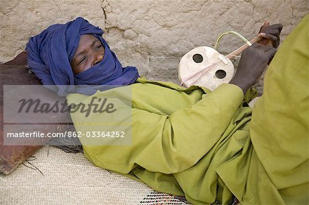 Mali,Timbuktu. A Tuareg man relaxes while playing his homemade stringed instrument at Timbuktu.