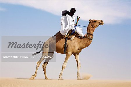 Timbuktu, Mali. In der Wüste nördlich von Timbuktu, ein Tuareg-Mann reitet sein Kamel auf einer Sanddüne lenkt er das Tier mit den Füßen.