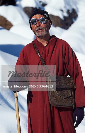 Marokko, hoher Atlas-Gebirge, Jebel Toubkal. Traditionelle Berber-Mann, gekleidet in Dj'laba und Schnee Brille zum Jebel Toubkal Ansatz auf das Tal von Ameln 4165m mit Neuschnee bedeckt.