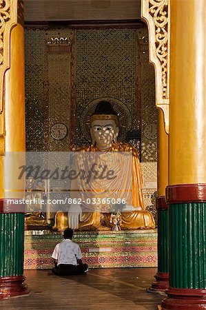 Myanmar, Birmanie, Yangon. Bouddhiste fervent prière au pied d'une statue de Bouddha dans le Temple d'or de Shwedagon complexes.