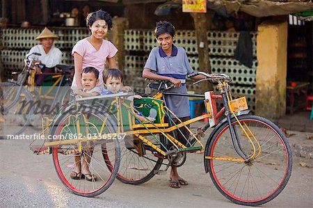 Myanmar,Burma,Sittwe. A Burmese family takes to the streets of Sittwe in a trishaw,a popular means of transport in which passengers sit back to back in a sidecar.