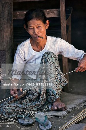 Myanmar, Burma, Mrauk U. Rakhine Frau raucht eine Cheroot wie sie Bambus in Bereitschaft, machen den Rahmen eines weiten Krempe, Bambus hat teilt.