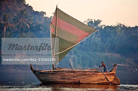 A large wooden boat of Rakhine design sails up the Lay Myo River in fading evening light.