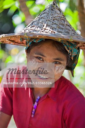 Myanmar,Burma,Rakhine State,Laung Shein. A girl from Laung Shein village wearing a wide-brimmed bamboo hat. Her face is decorated with Thanakha,a local sun cream and skin lotion.