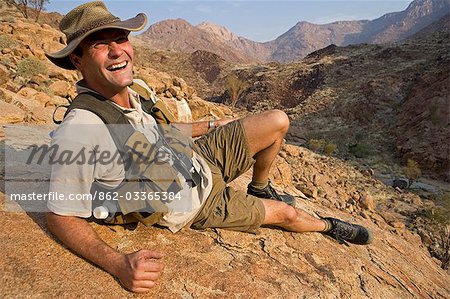 Namibia,Damaraland,Brandberg. Wildlife guide dressed in desert kharkis and bush hat,rests on a rock overlooking one of the many hidden valleys that surround Brandberg Mountain Namibia's higest peak.