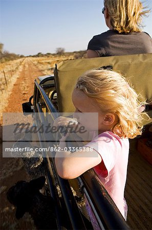 Région de Erongo Damaraland, Namibie. Une jeune fille, ses cheveux soufflant dans le vent, se penche sur le côté d'un véhicule de safari comme il pousse dans des pâturages sur une piste de jeu