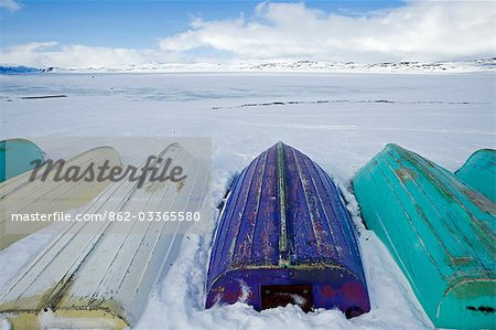 Troms, Norwegen Lyngen Alpen. Warten auf den Frühling beginnen die Multi farbige Rümpfe Sommer Fischerboote am Ende des Winters aus dem Schnee angezeigt werden.