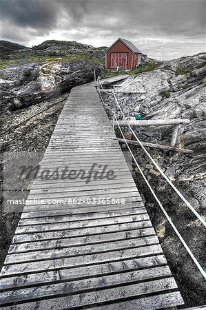 Norvège, Nordland, Helgeland. Un trottoir de bois entraîne un petit hangar à bateaux situé au-dessus des hautes eaux de la rive