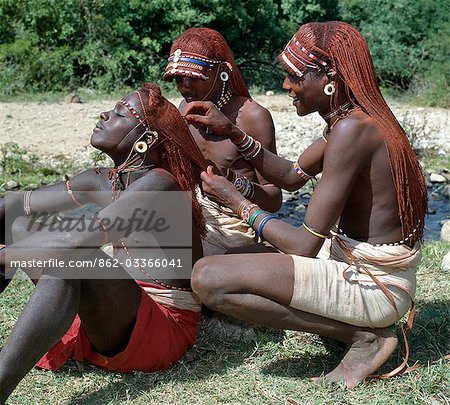 Two Samburu warriors dress the braids of a colleague. Long braids of Ochred hair distinguish warriors from other members of their society. The warriors are vain and proud,taking great trouble over their appearance. Round ornaments,often made of ivory,adorn the pierced and extended earlobes of warriors.