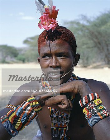 The adornments of Samburu warriors change from generation to generation. In the 1990's cheap plastic flowers from China became fashionable. This warrior is wearing several bracelets,which bear the Kenyan coat of arms.