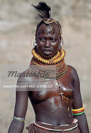 A Turkana girl in all her finery. Among the Turkana,cicatrization is a common form of beautification. She wears a crucifix given to her by a missionary; they are popular ornaments despite not necessarily being associated with Christianity.