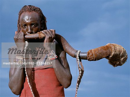 Un guerrier Masaï souffle une trompette de la corne d'un grand koudou. Le bracelet est orné de coquillages. Corne de koudou trompettes sont seulement sonne pour appeler les hommes à des armes ou les cérémonies.