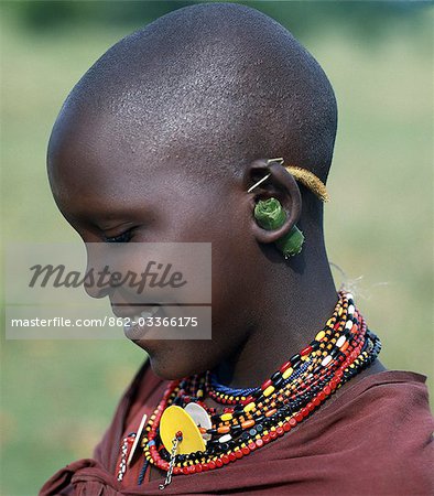 A young Maasai girl keeps the holes in her pierced ears from closing with grass and rolled leaves. She will gradually stretch her earlobes by inserting progressively larger wooden plugs. By tradition,both Maasai men and women pierce and elongate their earlobes for decorative purposes.