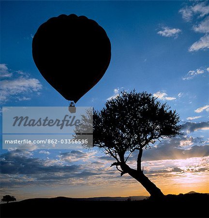 A hot air balloon takes off in Masai Mara Game Reserve as the sun rises over distant hills.