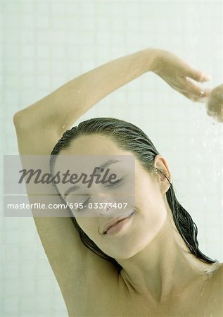 Woman taking shower, arms up and eyes closed