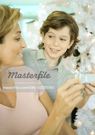 Boy handing mature woman present next to Christmas tree