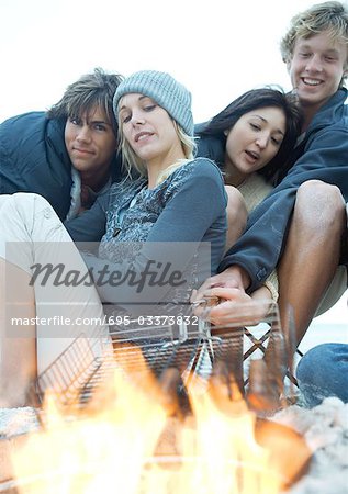 Jeunes adultes griller hot-dogs sur feu de camp