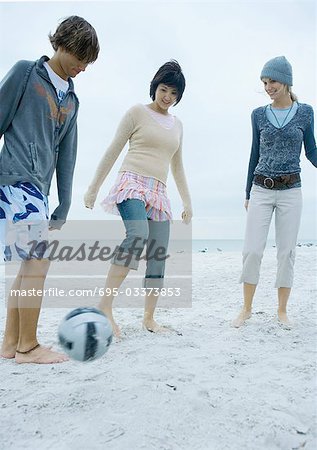 Three young adult friends playing soccer on beach