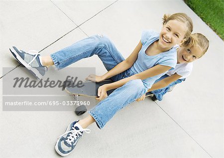 Two girls sitting on skateboard together