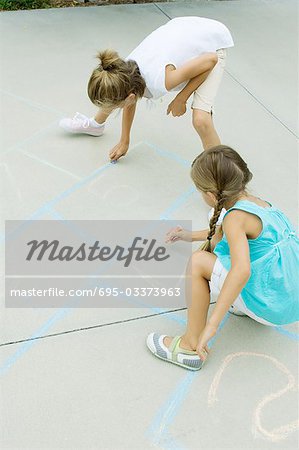 Girls drawing hopscotch game on driveway