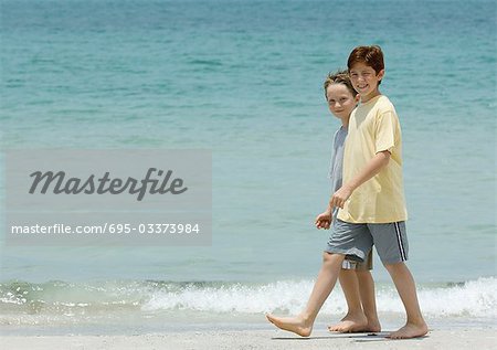 Boys walking next to surf on beach