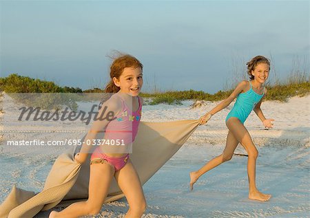 Two girls running on beach, holding blanket out in wind
