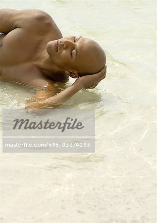 Man lying in shallow water with eyes closed