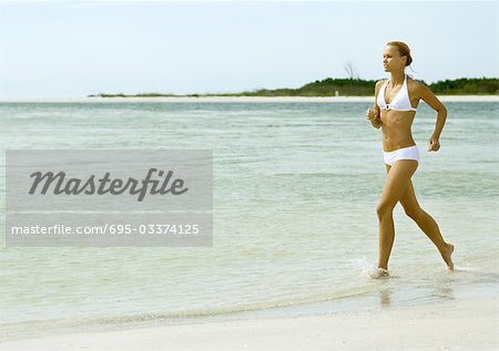 Frau im Bikini in der Brandung am Strand laufen