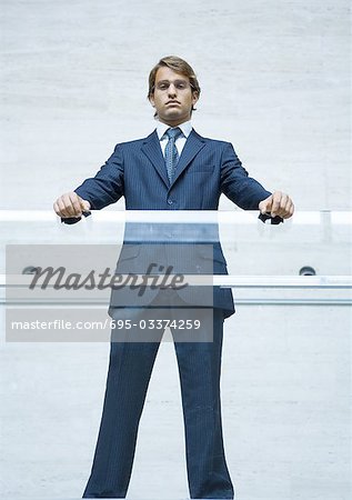 Businessman standing with hands resting on transparent guard rail, portrait, low angle view
