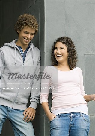 Young man and woman, leaning against corner of wall, laughing